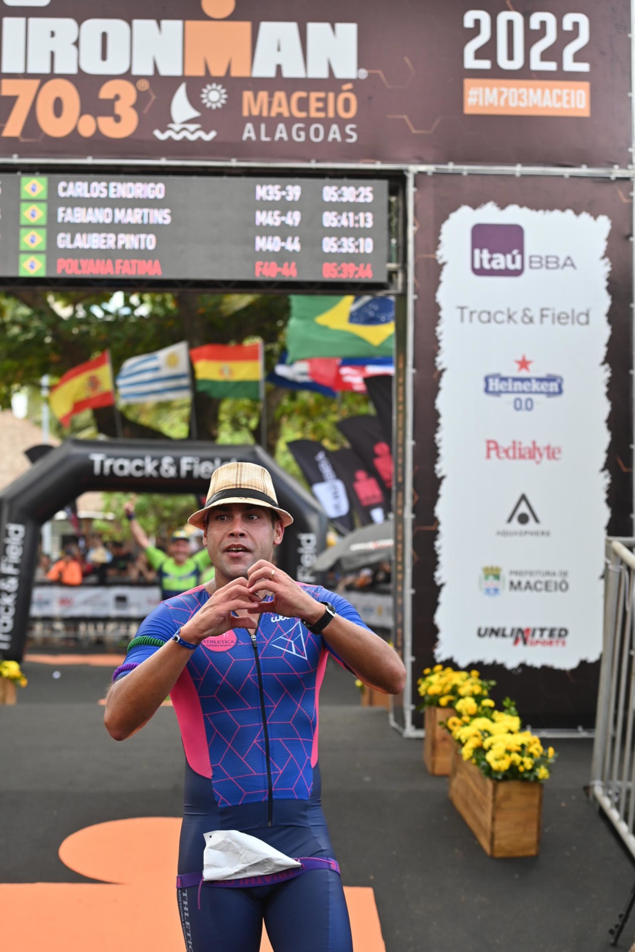 Carlos Endrigo cruzando a linha de chegada do IRONMAN 70.3 Maceió 2022, com nome e tempo no painel oficial